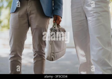 Two business colleagues standing outdoors holding a briefcase in casual office attire Stock Photo