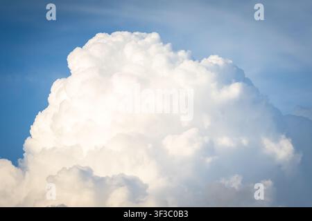 Sunlit cumulus rises like a bright mountain against blue sky its rounded peaks and flowing contours illuminated by warm light capturing the grandeur o Stock Photo