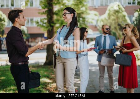 Business networking handshake between colleagues outdoors with professionals talking in the background Stock Photo