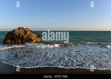 Sea stack on a pebble shore with incoming waves at sunset in Cyprus Stock Photo