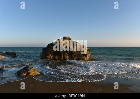 Sea waves crashing wildly over rocky boulders on a rocky dark sand shore, Cyprus Stock Photo