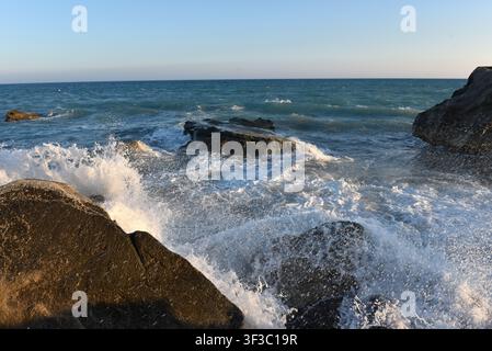 Sea stack on a dark sand shore with incoming white waves at sunset, Cyprus Stock Photo