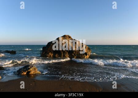 Sea stack on a pebble shore with incoming waves at sunset in Cyprus Stock Photo