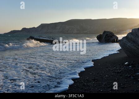 Sea stack on a pebble shore with incoming waves at sunset in Cyprus Stock Photo