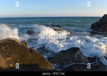 Sea stack on a pebble shore with incoming waves at sunset in Cyprus Stock Photo