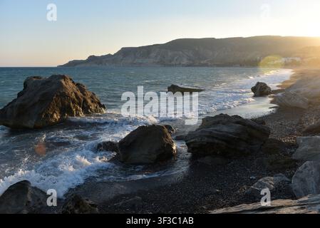 Sea waves crashing wildly over rocky boulders on a rocky dark sand shore, Cyprus Stock Photo