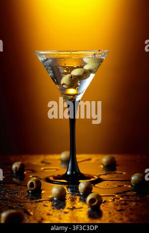 Green olives and glass of martini on a black stone table. Yellow backlight. Copy space. Stock Photo