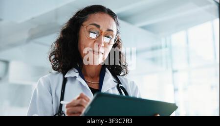 Doctor, woman and writing with tablet in hospital for insurance report, reading or scroll email. Mature, medical professional and digital tech for Stock Photo