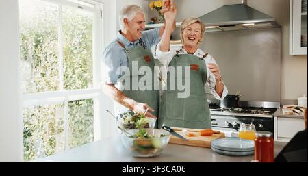 Cooking, fun and old couple in kitchen with dance, happy moment and bonding with culinary hobby. Smile, rhythm and senior people with meal prep Stock Photo