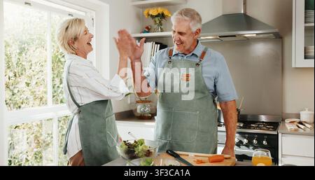 Senior, couple and cooking in kitchen with high five, bonding together and laugh for funny joke. Happy, married elderly people and celebration in Stock Photo