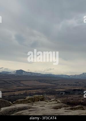 Mountain range with snow patches and cloudy sky viewed from rocky foreground. Stock Photo