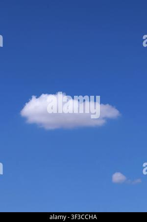 Singular cloud, against a clear blue sky. Perfect for themes of simplicity, minimalism and as a metaphor. Portrait size and digital photography. Stock Photo