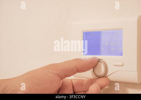 Close up view of mans hand adjusting digital thermostat controller dial on wall for home heating temperature efficiency and energy saving utility conc Stock Photo