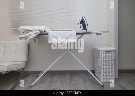 Ironing clothes on ironing board in modern home interior with laundry basket. Stock Photo