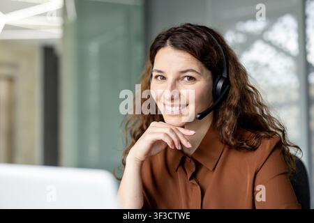 Smiling woman wearing a communication headset, providing helpful customer service and support in a professional office environment, symbolizing connection and online assistance Stock Photo