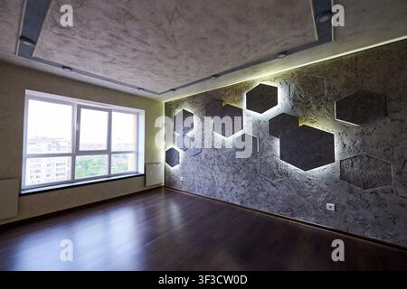 Spacious unfurnished interior with glowing geometric accent wall, textured ceiling and wooden floor. Bright residential room, home decor and real estate concept Stock Photo
