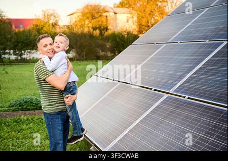 Father hugging son near solar panels. Happy family outdoors, renewable energy concept, clean technology, sustainable lifestyle and eco friendly future Stock Photo