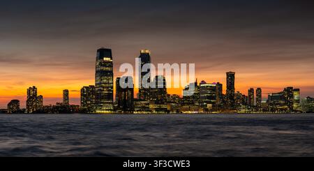 Downtown Jersey City skyline and Exchange Place at sunset with illuminated skyscrapers along the Hudson River. New Jersey, USA Stock Photo