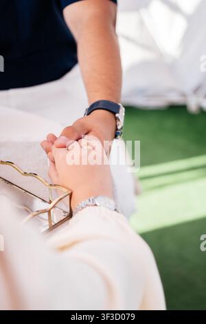 Engaged couple holding hands showing a diamond engagement ring in front of a bouquet of white roses, a romantic close up of love and marriage Stock Photo