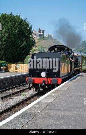 Corfe Castle, England July 18 2026. Steam train at Corfe Castle Station Dorset UK Passengers on board black smoke from engine Historic castle ruins Stock Photo