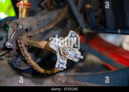 A rusty metal axle coupling with exposed castle nut and cotter pin on chain driven small engine, close up mechanical detail with oil residue and worn Stock Photo