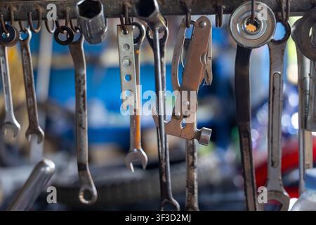 A rusty metal hand tools hanging on workshop rack with shallow depth of field, showing wrenches, pliers, sockets and hardware in gritty workshop atmos Stock Photo