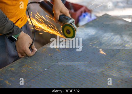 A worker using handheld angle grinder cutting steel plate, sparks flying, industrial workshop action shot with safety gear and focused motion Stock Photo