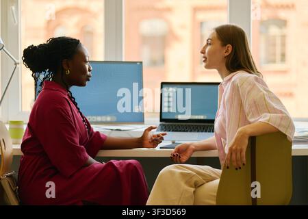 Black Woman and Adult Woman Discussing Project in Office Stock Photo