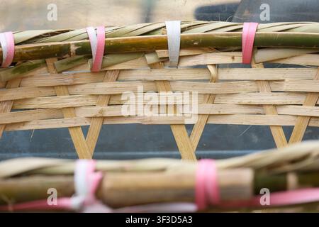 A woven bamboo basket rim with natural straw weave and colorful plastic ties showing rustic texture and handcrafted detail, warm tones and close up co Stock Photo