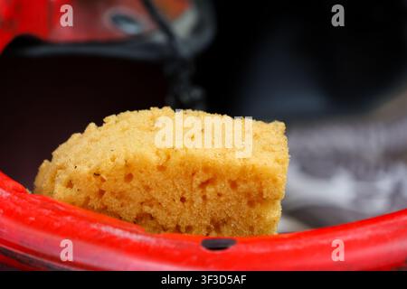 A yellow cleaning sponge resting on red bucket rim with soft texture and warm lighting conveying domestic chore mood Stock Photo