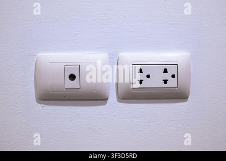 Close up photograph of a white wall plate with a double electric power socket and a coaxial TV antenna outlet on a clean white interior wall. Stock Photo