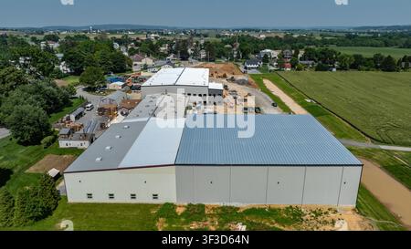 Workers are busy at a construction site where large buildings are being built. The buildings are located close to a small town surrounded by fields. Heavy equipment is visible nearby. Stock Photo