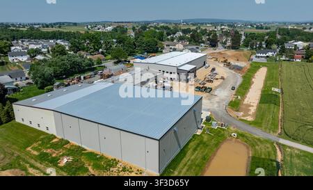 A construction site is busy with workers and machinery. New buildings are being put up among nearby houses. Open land surrounds the area, with fields visible in the background. Stock Photo