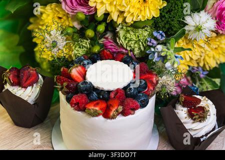 Frosted cake covered with strawberries, blueberries, and raspberries fills the frame against a colorful bouquet background, emphasizing texture Stock Photo