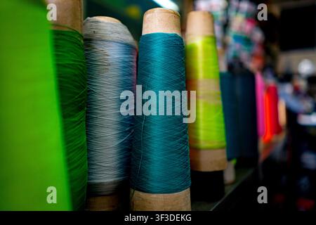 Vibrant colorful spools of industrial sewing thread lined up on a shelf in a tailor workshop or fabric store. Stock Photo