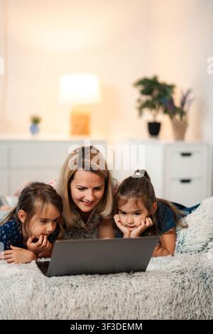 Mother and daughters watching laptop together on bed Stock Photo