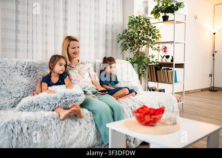Mother and daughters relaxing on sofa watching TV at home Stock Photo