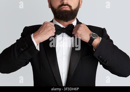 Cropped view of young man in formal suit adjusting bow tie on grey background, closeup Stock Photo