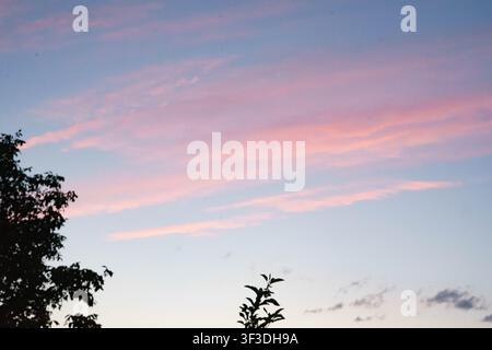 Pink clouds in the evening sky at sunset with soft pastel colors above the countryside landscape. Stock Photo