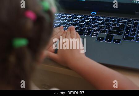 Child using a laptop computer at home. Close-up of children's hands typing on a keyboard during online learning or educational activities. Stock Photo