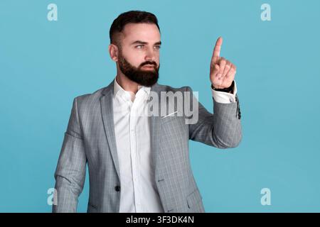 Handsome millennial business owner touching interactive screen on blue background, space for design Stock Photo