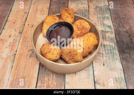 Crispy Chicken Nuggets Arranged Around Dark Dipping Sauce in Round Container on Rustic Wooden Table Stock Photo