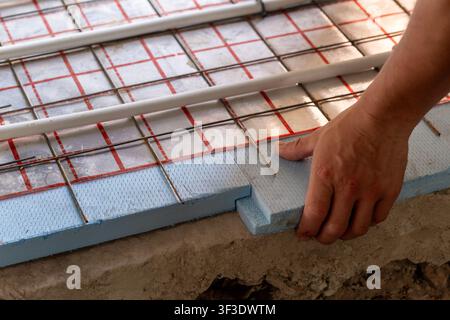 Detailed view of technician hands laying radiant heating pipes on foam board insulation. Modern plumbing installation and energy-saving building Stock Photo