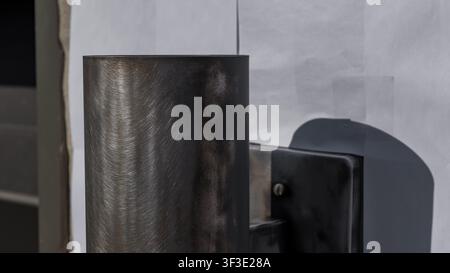 Modern cylindrical wall light fixture in a brushed metal finish is mounted on a textured wall surface, with white paper partially visible in the backg Stock Photo