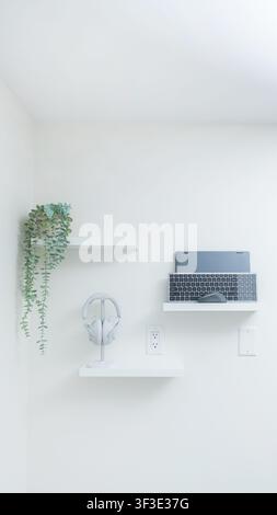 Minimalist workspace featuring a laptop, headphones, and a plant on white shelves against a bright wall in a contemporary interior design Stock Photo