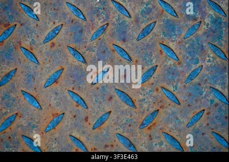 Close-up view of a worn, rusty diamond plate metal floor with a tread pattern. Dark industrial metallic background featuring anti-slip texture, rust spots, and rugged steel surface. Ideal for construction, engineering, safety, architectural, and grunge design concepts. Stock Photo