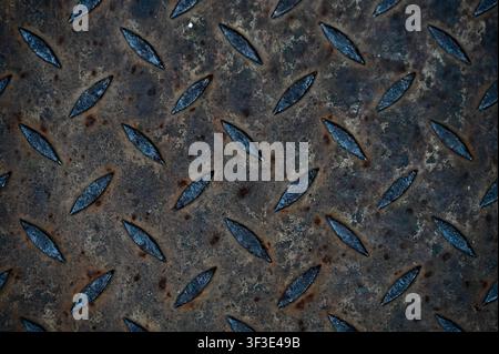 Close-up view of a worn, rusty diamond plate metal floor with a tread pattern. Dark industrial metallic background featuring anti-slip texture, rust spots, and rugged steel surface. Ideal for construction, engineering, safety, architectural, and grunge design concepts. Stock Photo