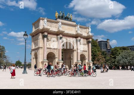 A guide with a group of tourists on bicycles in front of the 'Arc de Triomphe du Carrousel' a triumphal arch in the 1st arrondissement of Paris. Stock Photo