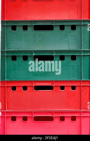 Front view close-up of colorful red and green plastic storage crates stacked vertically on top of each other. Bright geometric texture and pattern suitable for logistics, warehousing, transport, agriculture, recycling, container organization, and supply chain concepts. Stock Photo