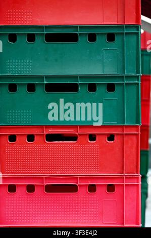 Front view close-up of colorful red and green plastic storage crates stacked vertically on top of each other. Bright geometric texture and pattern suitable for logistics, warehousing, transport, agriculture, recycling, container organization, and supply chain concepts. Stock Photo